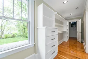 Spacious, light-filled walk-in closet featuring white shelves and drawers with hardwood floors.